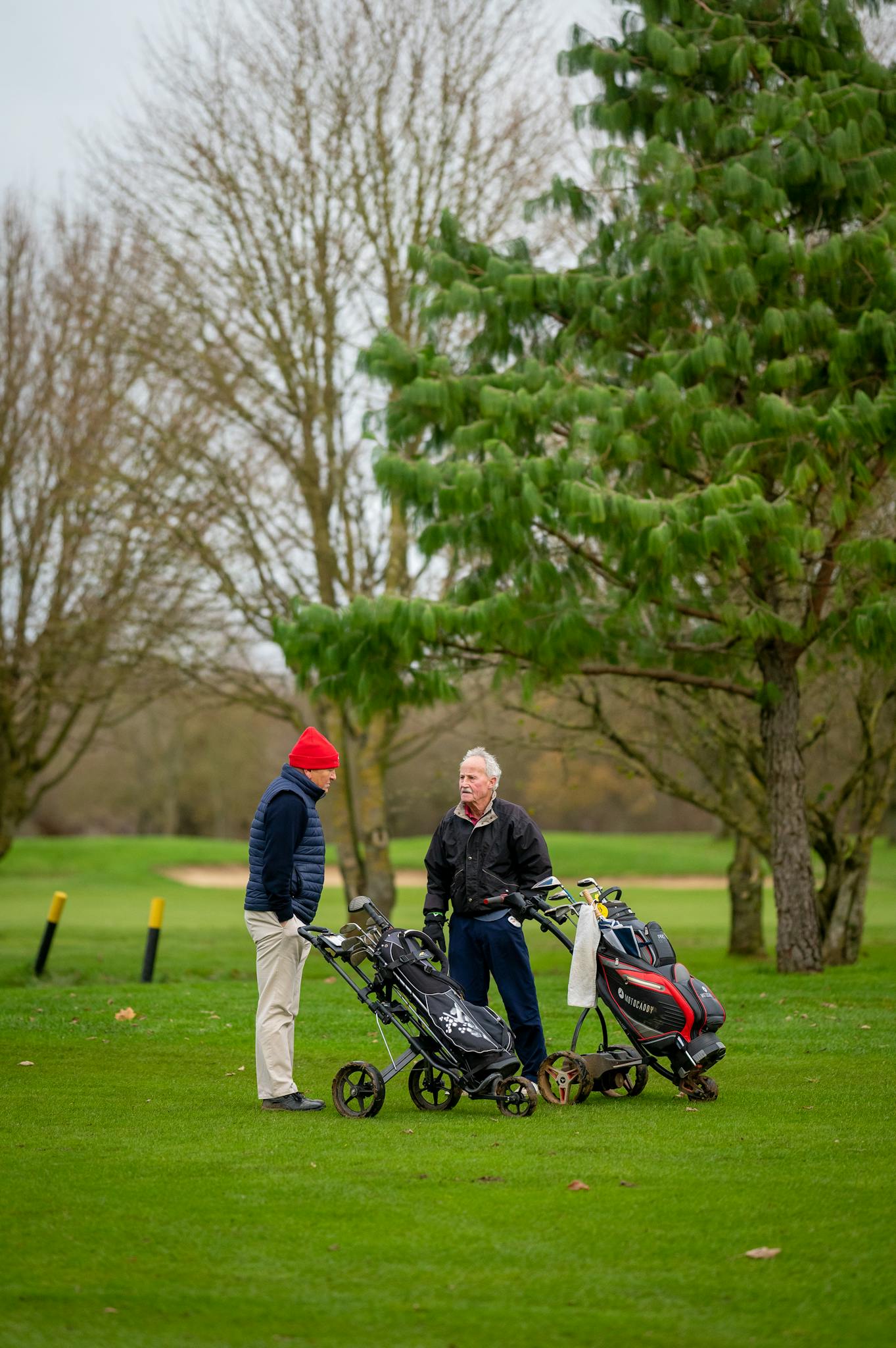 Two senior men engaged in conversation on a golf course with equipment nearby.